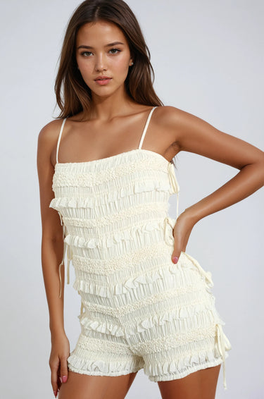 Textured knit romper with smocking, adjustable straps, and side ties. Light, breezy, and softly powerful.